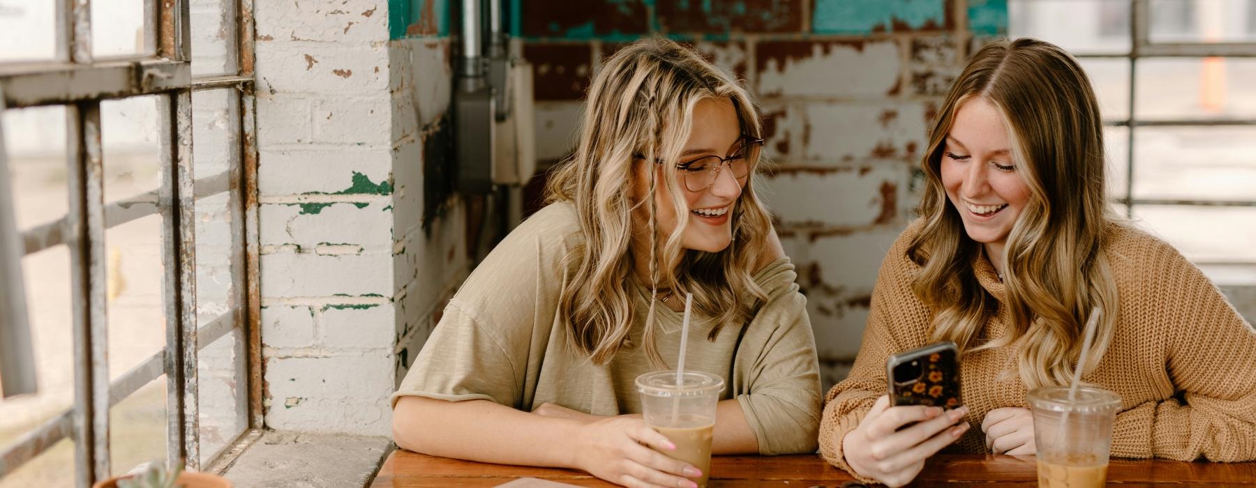 a couple of women sitting at a table looking at a cell phone